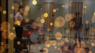 Grup arkadaşları gitar çalıyor, davul çalıyor ve mikrofona altın bokeh ile şarkı söylüyor. Müzisyenler, kayıt, performans, ses, eğlence, üretim, stüdyo