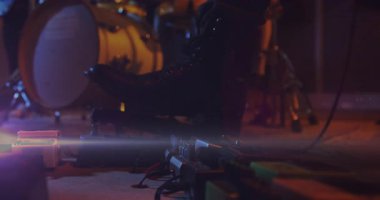 Sahnede kablolar arasında parlayan gitar efektleri pedalları ve 3 boyutlu bulanık davul donanımı. Müzisyen, performans, ekipman, müzikal, ışıklandırma, atmosfer, teknoloji