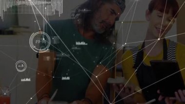 Ekip üyeleri atölyedeki tableti inceliyor, teknoloji ağı düğümleri ve dalga formu grafiklerini gösteriyor. İşbirliği, yenilik, veri görselleştirme, dijital tasarım, yaratıcı takım çalışması, diy, modern çalışma alanı