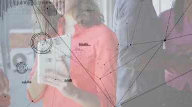Tablet tutan kadın, teknik ofisteki iş arkadaşlarıyla konuşuyor. Ağ grafikleri masanın üzerinde yüzüyor. İşbirliği, yenilik, dijital, takım çalışması, iletişim, modern, teknoloji