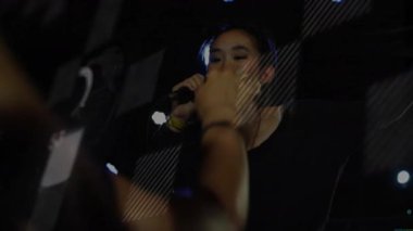 Konser sahnesinde bileklik takan şarkıcı dairesel grafik kaplamayı gösteriyor. Performans, eğlence, canlı, enerjik, gece hayatı, konser, müzik