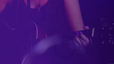 Sahnede gitar çalan bayan müzisyen, müzik pazarlaması için mor ışıkla kaplanmış neon kaplamalar. Performans, eğlence, konser, canlı, yaratıcı, gece hayatı, modern