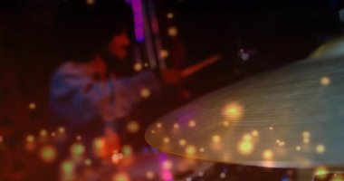 Davulcu müzik prodüksiyonu sırasında canlı ses dalgaları ve renkli bokeh simgeleriyle zil çalıyor. Perküsyon, canlı performans, sahne aydınlatma, müzik aleti, konser, canlı, ses