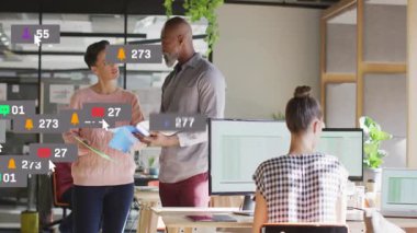 Modern iş ofisindeki belgeleri inceleyen iki iş arkadaşı yüzen sosyal medya simgeleri sergiliyor. İşbirliği, üretkenlik, takım çalışması, modern, kurumsal, çalışma alanı, teknoloji