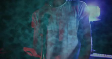 Erkek şarkıcı, müzik pazarlaması için animasyon dumanı arasında sahnede mikrofon kullanarak şarkı söylüyor. Performans, konser, eğlence, atmosfer, canlı, dramatik, dinamik