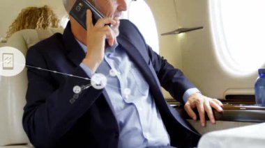 İş CEO 'su özel jetiyle akıllı telefondan konuşuyor. Kabini dijital müzik telefon ikonları kaplıyor. Şirket, lüks, teknoloji, yönetici, seyahat, bağlantı, sofistike