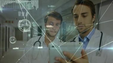Tıp koridorundaki tableti inceleyen iki erkek doktor yüzen veri örtüsü grafikleri gösteriyor. Tıp, sağlık, teknoloji, profesyonellik, teşhis, yenilik, takım çalışması