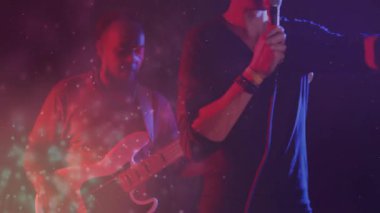 Müzik grubu arkadaşları, mikrofon tutan şarkıcı, animasyon parçacık ışıkları altında çalan gitarist. Göstericiler, konser, canlı, sanatsal, eğlence, sahne, dinamik