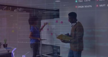 Kadın beyaz tahtayı işaret ediyor ve erkek ofiste iş birliği yapıyor. Finans tablolarını gösteriyor. İş, takım çalışması, yenilik, modernlik, iletişim, üretkenlik, veri