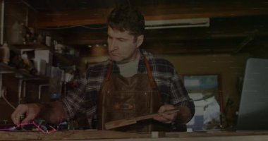 Marangoz tezgahta ahşap şerit ölçüyor, finans veri tablosu örtülerini gösteriyor. Zanaatkar, atölye, marangozluk, kesinlik, aletler, işçilik, kırsal