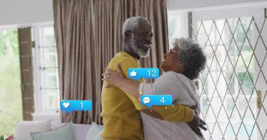 Son sınıf çifti oturma odasında kucaklaşıp sosyal medya simgelerini gösteriyorlar. Romantizm, arkadaşlık, sıcaklık, emeklilik, evcil, konfor, pozitiflik