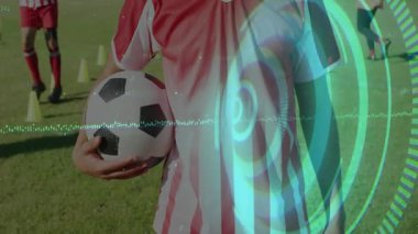 Futbol oyuncusu spor antrenman sahasında topu tutarken, animasyon istatistikleri konilerin üzerinde yükselen grafikler çiziyor. Atletik, takım çalışması, açık hava, canlı, rekabetçi, fitness, spor