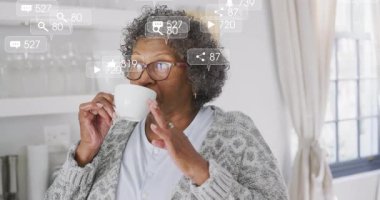 Üst düzey kadın, parlak mutfakta kahve yudumluyor, yüzen dijital pazarlama bildirim simgeleriyle. Yaşlılık, sağlık, yaşam tarzı, modern, dijital, konfor, yerli