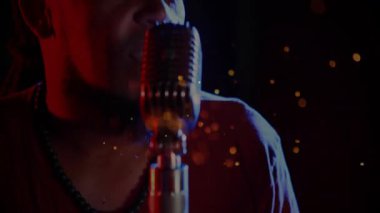 Erkek şarkıcı sahne ışıkları altında mikrofona performans sergiliyor, yüzen parçacıklar müzik havasını yükseltiyor. Klasik, konser, dramatik, renkli, performans, sanatsal, akustik