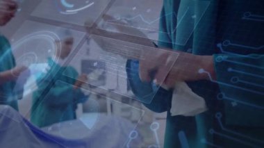 Cerrahın elinde 3D çizelge gösteren el bilgisayarı var. Meslektaşları ameliyathanede verileri izliyor. Tıbbi, teknoloji, yenilik, sağlık, fütürizm, profesyonellik, veri