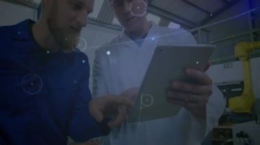 Endüstriyel fabrikada tableti analiz eden teknisyen ve mühendis, veri örtüleri, robotik kol gösteriyor. Teknoloji, yenilik, işbirliği, imalat, otomasyon, endüstri, makine