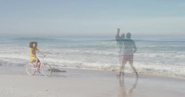 Dans eden çiftlerle ve pazarlama için okyanus dalgalarıyla sahil şeridinde pembe bisiklet süren bir kadın. Kıyı, eğlence, sükunet, bağbozumu, ahenk, yansıma, yaşam tarzı