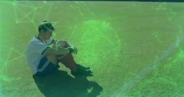 Çim sahasında oturan bayan futbolcu, spor teknolojisi için dijital ağ örtüsü gösteriyor. Sporcu, fitness, açık hava, canlı, yenilik, takım çalışması, rekabet