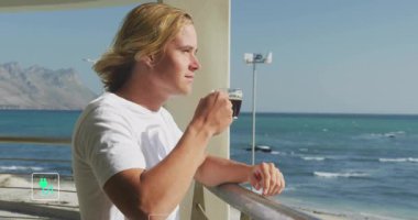 Okyanusa bakan balkonda kahvesini yudumlayan bir adam yüzen yeşil sürdürülebilirlik simgeleri gösteriyor. Deniz manzarası, sürdürülebilirlik, çevre dostu, yenilenebilir, çevre bilinci, modern