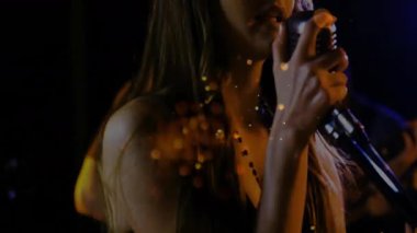 Kadın şarkıcı, canlı turuncu bokeh ve mavi kirişlerle sahnede tutkuyla müzik yapıyor. Vokalist, performans, konser, sanatsal, ışıklandırma, atmosfer, eğlence