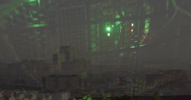 Şehir manzarasını kaplayan bal peteği ızgarası parlayan yeşil LED fanları ve soğutma kablolarını gösteriyor. Teknoloji, metropol, modern, yenilik, elektronik, altyapı, aydınlatma