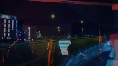 Bando, yansıtıcı pencereden canlı müzik eşliğinde mikrofon ve arabanın ışık izlerini örtüyor. Performans, şehir, gece hayatı, müzik, yansıtıcı, canlı, ambiyans