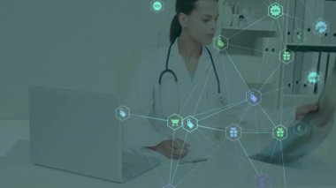 Masasında dizüstü bilgisayarla röntgeni inceleyen kadın doktor, alışveriş ikonlarıyla sağlık teknolojisi gösteriyor. Tıbbi, teknoloji, profesyonel, tanı, sağlık, dijital, modern