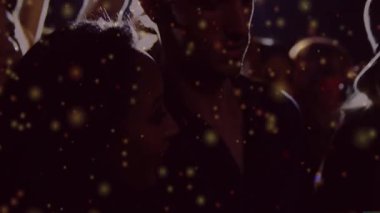 Karanlık bir partide dans eden üç arkadaş, yüzen altın bokeh ışıltıları sergiliyorlar. Gece hayatı, kutlama, yoldaşlık, canlı, çevresel, genç, enerjik.
