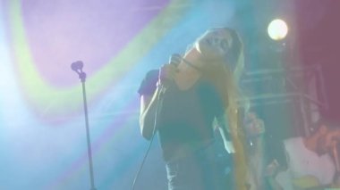 Müzik endüstrisi sahnesinde şarkı söyleyen kadın şarkıcı, kirişleri üzerinde animasyon ses dalgası ikonlarıyla. Performans, müzik, gece hayatı, eğlence, sahne, canlı, dinamik