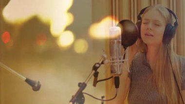 Müzik stüdyosunda şarkı söyleyen kadın vokalist, kulaklıklar ve ses dalgalarıyla mikrofon etrafında dolaşıyor. Müzik, kayıt, vokal, performans, ses, profesyonel, sanatsal