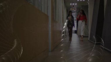 İki meslektaş, kahve fincanlarının üzerinde yüzen animasyon çizelgeleriyle iş koridorlarında yürüyor. Ofis, işbirliği, modern, profesyonel, içişleri, ağ oluşturma, kurumsal