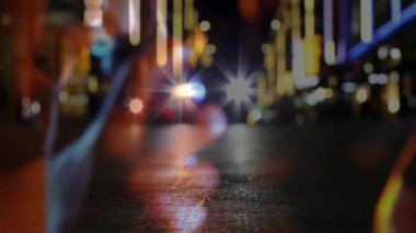 Neon ışıklı teknoloji caddesinde, farların üzerinde çizgi çizgileri olan akıllı telefonu kavrayan içerik yaratıcısı. Teknoloji, şehir, gece manzarası, modern, canlı, fütüristik, yansıtıcı