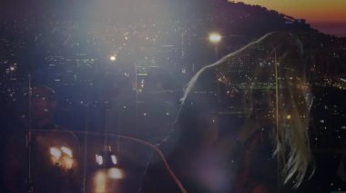 Gece loş ışıklı stüdyoda şarkı söyleyen müzik ikilisi şehrin yansımalarına karşı klasik mikrofonu gösteriyor. Şehir, gece hayatı, performans, ambiyans, sanatçılık, canlı, yaratıcı