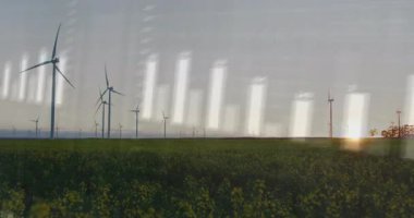 Yeşil alanda, şeffaf veri örtüsü, çubuk grafikleri ve dalga biçimleriyle rüzgar türbinleri görselleştiriliyor. Yenilenebilir, sürdürülebilirlik, teknoloji, enerji, fütürizm, çevre, yenilik