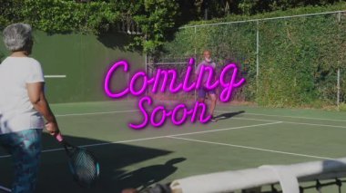 Tenis oyuncuları, neon pembesinin yakında pazarlama için üst üste geldiği güneşli sahada yürüyüş yapıyorlar. Atletik, spor, yarışma, açık hava, canlı, boş zaman, eğlence