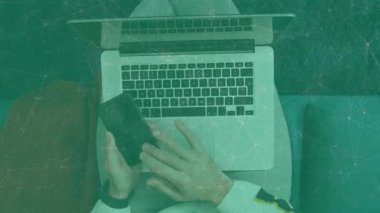 Adam oturma odasında dizüstü bilgisayar ve akıllı telefon kullanıyor. Animasyon finans çizelgeleri ve simgeler sergiliyor. Teknoloji, çalışma alanı, modern, gündelik, dijital, yaşam tarzı, konfor