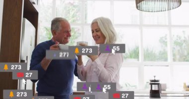 Son sınıf çifti, pazarlamayı gösteren sosyal medya simgeleriyle mutfakta kahve yudumluyorlar. Yaşam tarzı, refah, modern, iç mekan, iletişim, bağlantı, eğlence