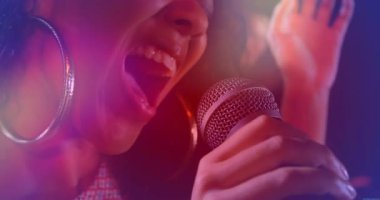 Müzik endüstrisi şarkıcısı, kırmızı-mor ışıklar altında, animasyon ses dalgaları ile sahnede performans sergiliyor. Performans, konser, sahne, aydınlatma, enerji, eğlence, vokal