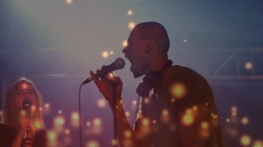 İkili, renkli spot ışıkları altında müzik sahnesinde, mikrofonlar etrafında animasyon dengeleyiciler ile performans sergiliyor. Müzisyenler, performans, canlı, eğlence, gece hayatı, sahne sanatları, enerji