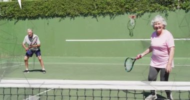 Dışarıda tenis oynayan son sınıf çifti, hareketli spor grafikleriyle raketleri, ağı ve çemberi gösteriyor. Atletizm, fitness, aktif, boş zaman, sağIık, canlı, açık hava