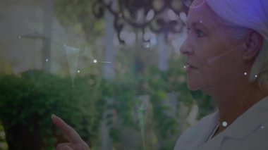 Kıdemli kadın bahçede holografik dairesel HUD arayüzü gösteriyor, teknolojik arayüz tasarımı gösteriyor. Gelecekçi, yenilikçi, teknoloji, konut, açık hava, canlı, bağlantı