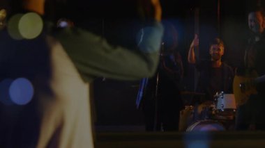 Erkek DJ yapımcı, müzik prodüksiyonunun ışıkları altında, animasyon ses dalgalarıyla sahnede kollarını kavuşturuyor. Performans, konser, müzik, işbirliği, gece hayatı, stüdyo, dinamik