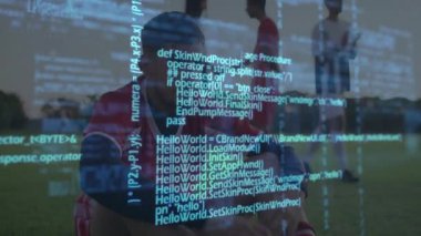 Erkek futbolcu çim sahada oturuyor, yüzen veri grafiklerini gösteren bir spor stratejisi uyguluyor. Atletik, takım çalışması, yoldaşlık, açık hava, canlı, rekabetçi, pozitif