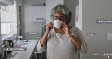 Modern mutfakta kahvesini yudumlayan son sınıf öğrencisi bir kadın, sosyal medya tebligatları etrafta beliriyor. Yaşlılık, sağlık, rahatlama, çağdaş, yaşam tarzı, dijital, konfor