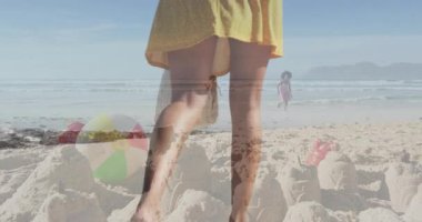 Anne dalgalara doğru yürüyor, çocuklar kumdan kalelerin üzerinde animasyon çizelgesiyle oynuyor. Tatil, aile, eğlence, açık hava, canlı, neşeli, rahatlama.