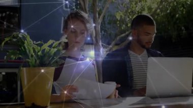 İş arkadaşları masada dizüstü bilgisayarlarını ve kahve fincanlarını paylaşıyor, parlayan teknoloji ağları sergiliyorlar. İşbirliği, çalışma alanı, modern, bağlantı, yeşillik, takım, yenilik