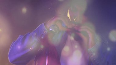 Kot ceket giyen bir müzisyen mor sis ve bokeh altında mikrofona mızıka çalıyor. Müzisyen, canlı performans, atmosfer, bohem, bağımsız, yaratıcı, sahne sanatları