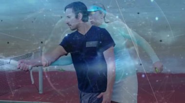 Erkek antrenör, kadın stajyere kil sahada rehberlik ediyor. Tenis verileri üst üste biniyor. Atletizm, akıl hocalığı, eğitim, dijital, spor, açık hava, odaklanma