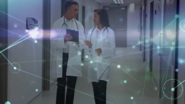 Hastane koridorunda yürüyen iki doktor, tabletteki hasta verilerini ağ grafikleriyle kontrol ediyor. Tıbbi, sağlık, dijital, modern, işbirliği, teknoloji, profesyonellik