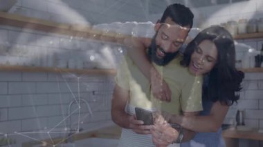 Modern mutfakta akıllı telefon kullanırken sarılan çift akıllı ev ağı grafikleri sergiliyor. Çağdaş, samimiyet, teknoloji, yaşam tarzı, yerli, sıcak, bağlantı